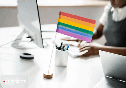 Blurred image of workplace desk with small LGBTQ2+ flag sitting on the desktop.